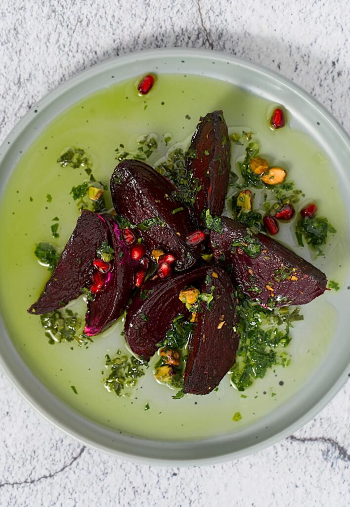 Healthy beet salad with pomegranate seeds and herbs on a green plate.