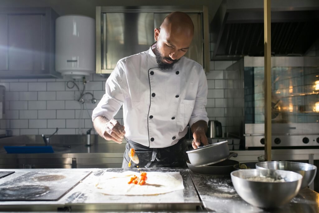 A skilled chef in uniform preparing dough in a professional kitchen setting.